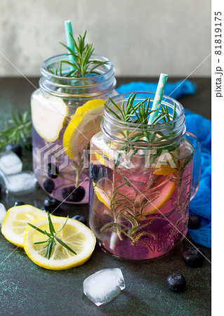 Lemonade or cocktail with blueberries and rosemary, cold refreshing drink with ice on dark concrete or stone table. 81819175