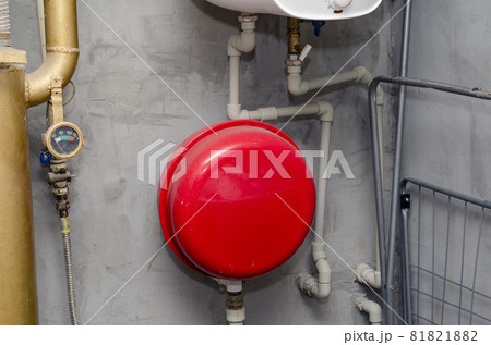 Boiler Room. Red expansion tank, piping, valves, gauge, water heater boiler. Gray plaster walls. Inside the room. Selective focus. 81821882