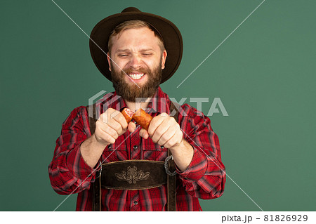 Portrait of bearded man in traditional Bavarian costume with sausages having fun isolated over green background. Oktoberfest, festival, traditions concept Portrait of bearded man in traditional Bavarian costume with sausages having fun isolated over green background. Oktoberfest, festival, traditions concept 81826929