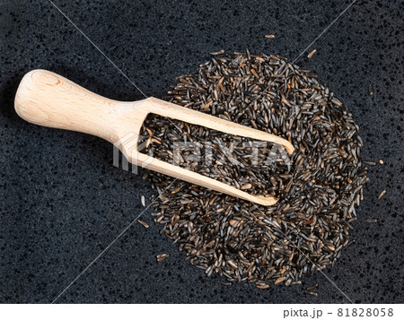 top view of wood scoop on pile of niger seeds (Guizotia Abyssinica) on black plate top view of wood scoop on pile of niger seeds (Guizotia Abyssinica) on black plate 81828058