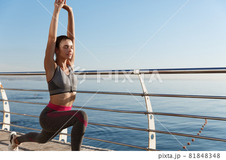 Outdoor shot of sportswoman workout near the sea. Woman workout or doing yoga exercises at the seaside promenade 81848348