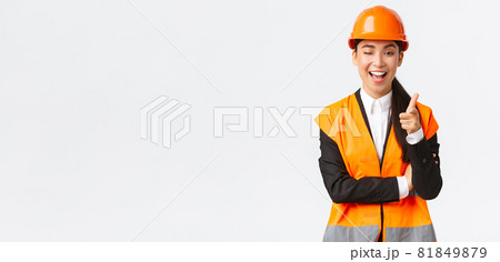 Smiling professional asian female construction manager in safety helmet and reflective jacket inviting check-out new building, wink and pointing finger at camera, showing client best estate Smiling professional asian female construction manager in safety helmet and reflective jacket inviting check-out new building, wink and pointing finger at camera, showing client best estate 81849879