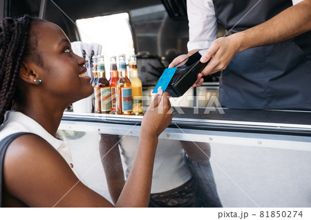 Close up of smiling woman paying with a credit card while standing at a food truck Close up of smiling woman paying with a credit card while standing at a food truck 81850274