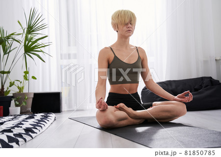 Woman sitting at home at the floor in lotus position Woman sitting at home at the floor in lotus position 81850785