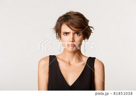 Close-up of timid angry cute girl, sulking and looking offended, standing over white background Close-up of timid angry cute girl, sulking and looking offended, standing over white background 81851038