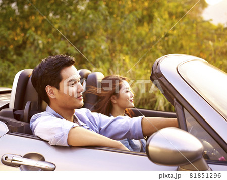 young asian couple riding in a convertible sport car at sunset. 81851296