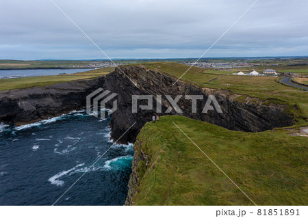 Aerial view of unrecognized people standing at edge of Moher Cliff in Ireland with sea waves hitting rocks during evening under cloudy sky 81851891
