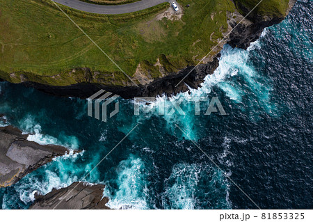 Birds eye view of Cliff in Ireland with car parked at end street on mountain with waves hitting the rocks during day Birds eye view of Cliff in Ireland with car parked at end street on mountain with waves hitting the rocks during day 81853325