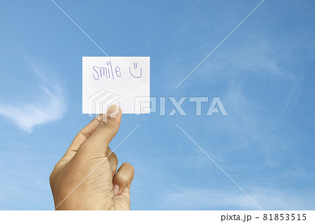 Hand holding smile word on paper card with blue sky background. 81853515