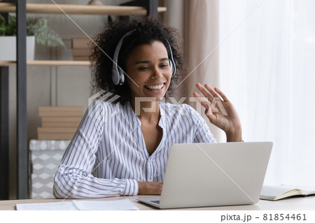 Confident biracial female in headset wave hand to laptop screen Confident biracial female in headset wave hand to laptop screen 81854461