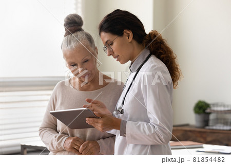 Serious GP doctor showing tablet screen to old female patient Serious GP doctor showing tablet screen to old female patient 81854482