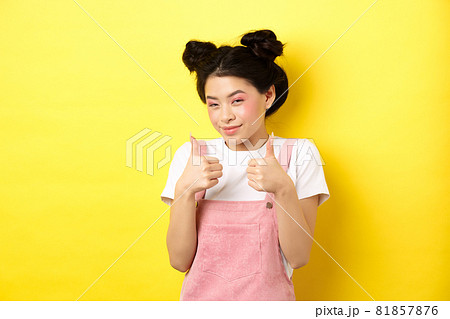 Cute teen asian girl with beauty makeup, showing thumbs up and smiling, praising and motivating you, making compliment, standing pleased on yellow background 81857876