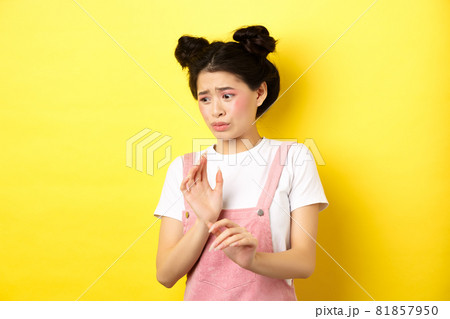 Disgusted asian girl raising hands up defensive, block something disgusting, turn away from aversion and reluctance, standing on yellow background 81857950