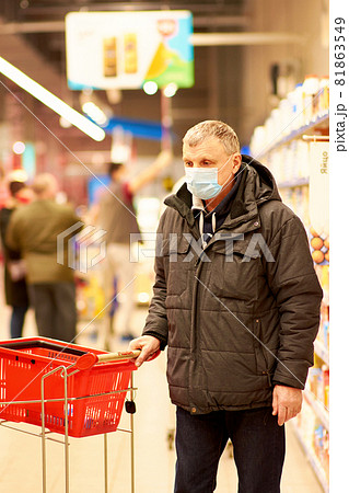 A 65-year-old man in a blue medical mask picks up groceries at a supermarket. A 65-year-old man in a blue medical mask picks up groceries at a supermarket. 81863549