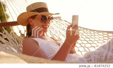 Working at sunset. Young happy female using smartphone while lying in the hammock on the beach 81874252