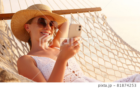 Working at sunset. Young happy female using smartphone while lying in the hammock on the beach 81874253