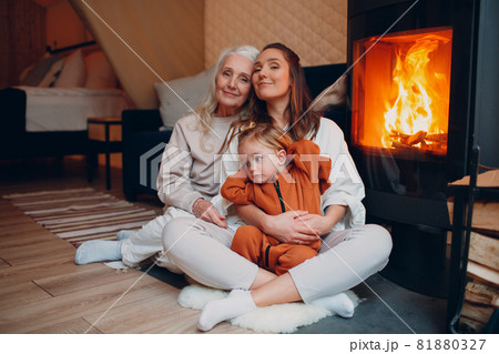 Grandmother, Mother and child sitting and playing on sofa near fireplace. Mom and baby. Parent with daughter and grandson little kid relaxing at home. Family having fun together. Mother's day. 81880327