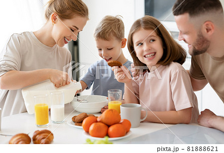 Young happy family with two cute little kids having breakfast together in kitchen and smiling 81888621