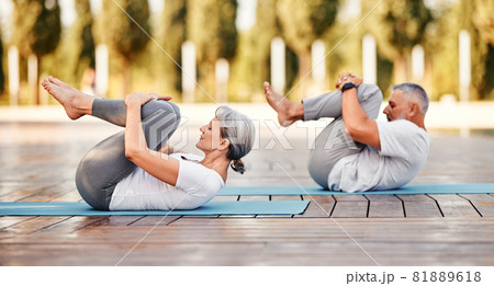 Senior couple  in sportswear lying on mat hugging her knees after yoga practice in park on sunny morning 81889618