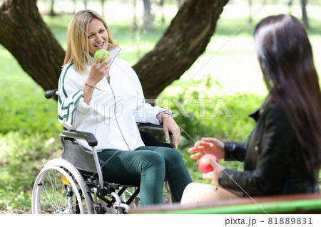 Disabled woman in wheelchair eating apple with her friend in park Disabled woman in wheelchair eating apple with her friend in park 81889831