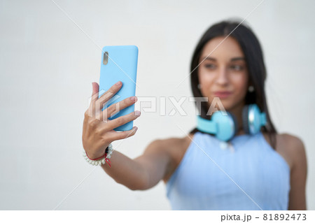woman taking a selfie with the smartphone with headphones on her neck 81892473