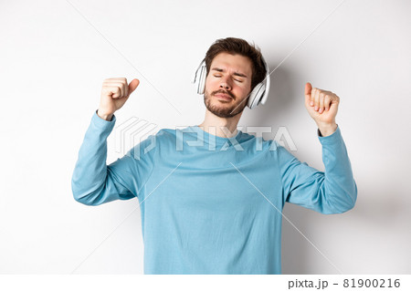 Happy handsome man dancing to music in headphones, listening songs and smiling, standing over white background Happy handsome man dancing to music in headphones, listening songs and smiling, standing over white background 81900216