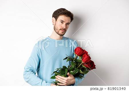 Handsome young man holding beautiful red roses for his lover on Valentines day, looking pensive, standing over white background 81901340