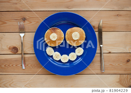 Pancakes with smile on blue plate and wooden background. banana fruit smiling - fun food for kids 81904229