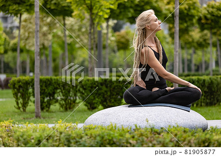 Young beautiful woman with blonde hair doing yoga exercise in green public park in summer morning, outdoors. Healthy lifestyle, mental health concept. Young beautiful woman with blonde hair doing yoga exercise in green public park in summer morning, outdoors. Healthy lifestyle, mental health concept. 81905877