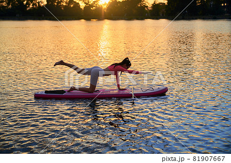 Woman practicing yoga on sup board during summer sunset Woman practicing yoga on sup board during summer sunset 81907667
