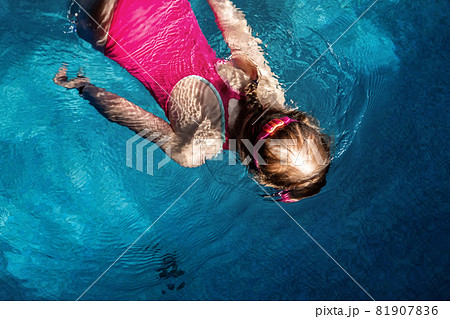 Above top view of little cute kid girl in sport pink swimsuit and goggles diving underwater in clear blue water of indoor swimming pool at dark evening time. Children watersport healthy activities Above top view of little cute kid girl in sport pink swimsuit and goggles diving underwater in clear blue water of indoor swimming pool at dark evening time. Children watersport healthy activities 81907836