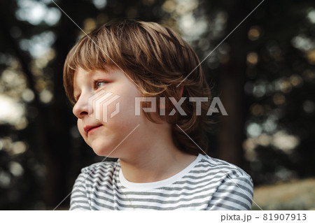 Portrait of cute boy in the forest thoughtfully looking afar. Blue eyed school kid day dreaming in the park. Relaxing outdoors 81907913