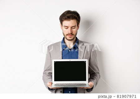 Handsome caucasian businessman in suit showing empty laptop screen, demonstrate promo, standing on white background 81907971