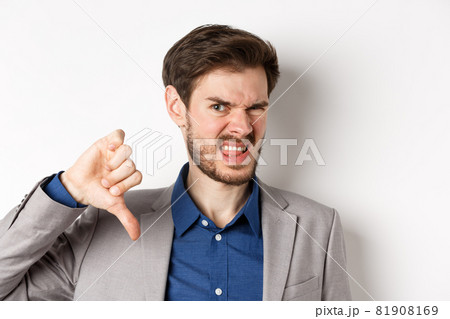 Close-up of disgusted guy in suit grimacing upset, showing thumbs down, express negative emotion, white background 81908169