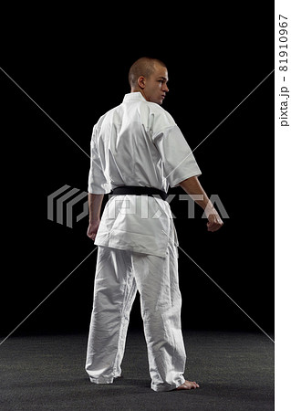 Back view full-length portrait of male sportsman in white kimono with black belt isolated over dark background Back view full-length portrait of male sportsman in white kimono with black belt isolated over dark background 81910967