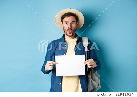 Excited tourist in straw hat, holding empty piece of paper and looking amused, going on summer travel, standing on blue background 81911034