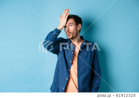 Annoyed man making facepalm and roll eyes from something stupid, standing over blue background with hand on forehead 81912320