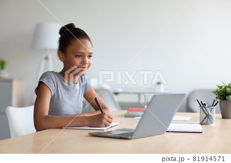 Smiling pretty smart teen african american girl student studying at home, watching online lesson on laptop 81914571