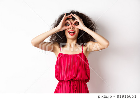 Impressed young woman seeing cool thing, look through hand binoculars and say wow, standing amazed at white background 81916651