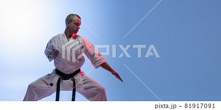 Cropped portrait of caucasian sportsman standing in a fight pose isolated over gradiet white blue background. Karate, judo, taekwondo sport 81917091