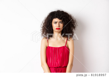 Sad frowning lady in red dress complaining, looking jealous or lonely, standing upset over white background 81918997