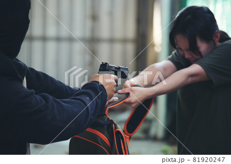 Thief armed man rob woman by gun on street so scared shocked face. Frightened asian woman was rob aggressive by danger bandit man. Robbery thief using gun burglar. Criminal aggression crime concept. 81920247