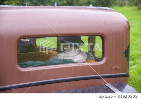An elderly woman in hat and raincoat is driving in old vintage retro car in brown colours. Grandmather with umbrella behind rear rectangular window of the antique old automobile under the rain An elderly woman in hat and raincoat is driving in old vintage retro car in brown colours. Grandmather with umbrella behind rear rectangular window of the antique old automobile under the rain 81920505