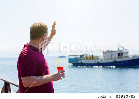 A man on a pier by the sea with a smile waves to a passing ship 81920785