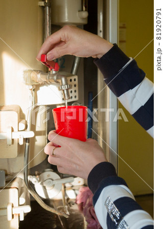 A woman on the train carefully pours boiling water into a red mug A woman on the train carefully pours boiling water into a red mug 81920791