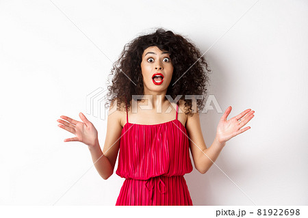 Excited woman with curly hair, talking with amazed face, explain big news, shaking hands and look astonished at camera, white background 81922698