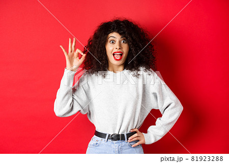 Excited pretty woman say yes, showing okay gesture and looking enthusiastic, agree or like something, making compliment, standing on red background Excited pretty woman say yes, showing okay gesture and looking enthusiastic, agree or like something, making compliment, standing on red background 81923288