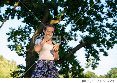 Girl phone. Euphoric screaming young girl holding smartphone showing winner gesture at sunny day in park. Messaging, being happy to text. Girl phone. Euphoric screaming young girl holding smartphone showing winner gesture at sunny day in park. Messaging, being happy to text. 81923724
