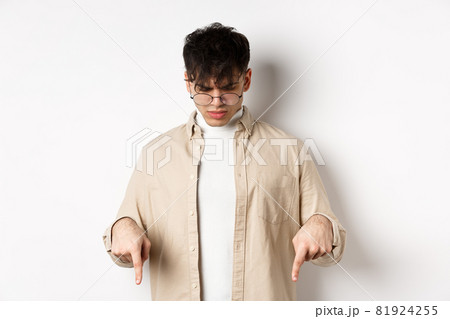 Confused frowning guy in glasses looking, pointing fingers down at something strange, standing puzzled on white background Confused frowning guy in glasses looking, pointing fingers down at something strange, standing puzzled on white background 81924255
