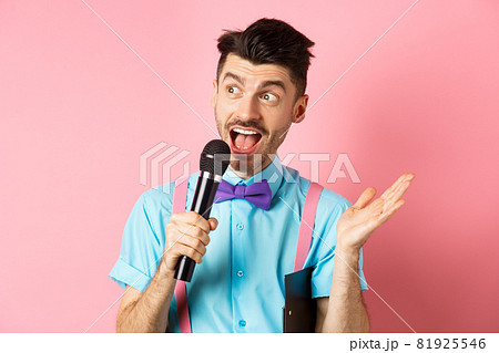 Image of male show host making speech, talking in microphone with clipboard under armpit, enteratin people on festive event, standing over pink background Image of male show host making speech, talking in microphone with clipboard under armpit, enteratin people on festive event, standing over pink background 81925546